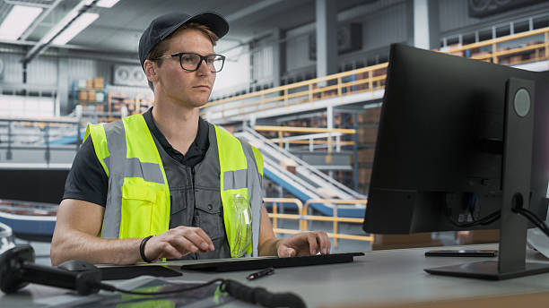 istock Male Stocking Manager Checking Inventory On Desktop Computer In Warehouse Facility With Automated Conveyor Belt. Logistics Company Employees Carrying Boxes to Package Products And Deliver to Clients. 2204713366