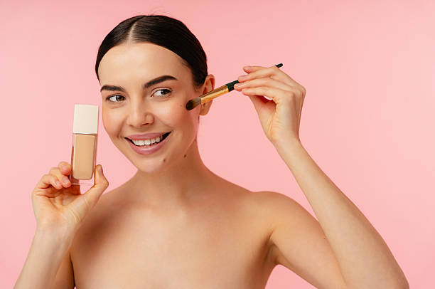 istock Smiling Person Applying Makeup Foundation With Brush Against Pink Background 2204722200