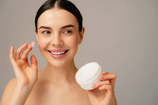 istock Smiling Woman Applying Cream to Face in Brightly Lit Studio Setting 2204724075