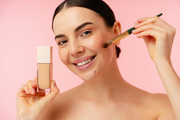 istock Smiling Person Applying Liquid Foundation with Makeup Brush on Pink Background 2204725041