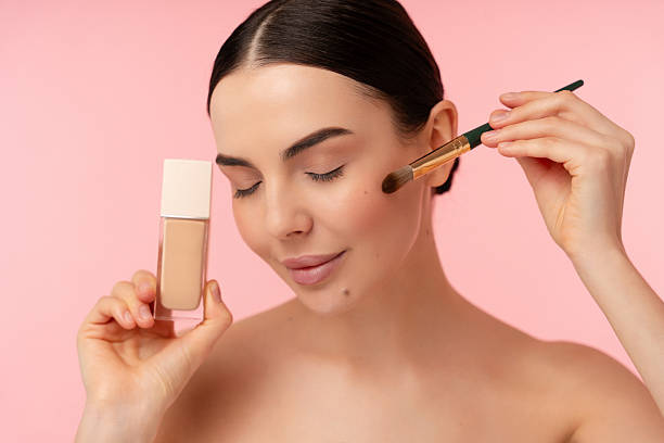 istock Woman Applying Liquid Makeup with Brush on Pink Background 2204726834