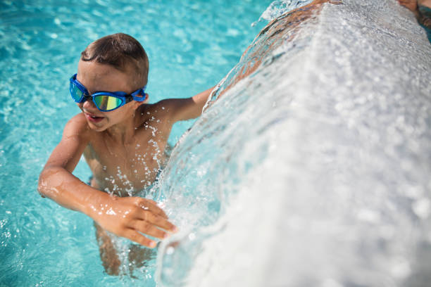 istock Happy little boy playing in swimming pool, climbing on a waterfall wall 2204727602