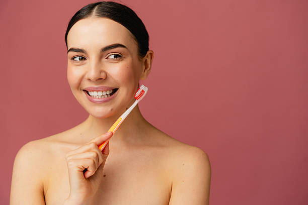 istock Smiling Woman Brushing Teeth Against a Vibrant Pink Background 2204728590