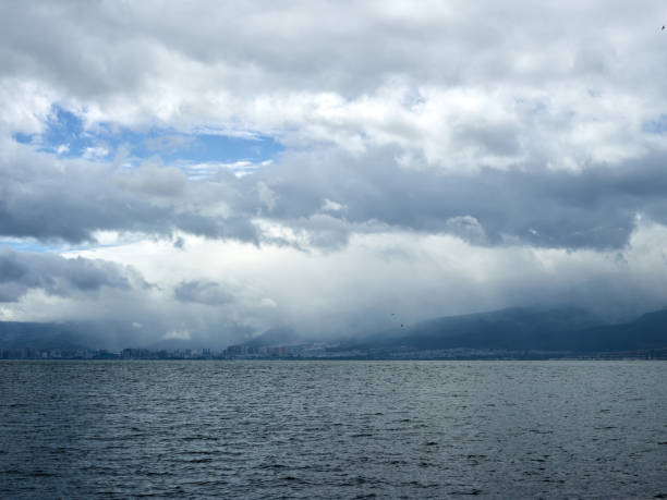 This photograph was taken at Erhai Lake in Yunnan, China, capturing the magnificent scene before an approaching storm. Heavy storm clouds blanket the distant mountains, while rays of sunlight pierce through the sky, casting ethereal beams onto the lake and land below. The image creates a dramatic contrast between the power of nature and its serene beauty. This compelling composition is perfect for landscape photography, weather phenomena, or nature-themed visual content.
