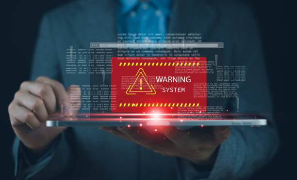 istock A businessman holds a tablet displaying a digital warning alert, emphasizing technology and security issues in modern systems. 2204734450