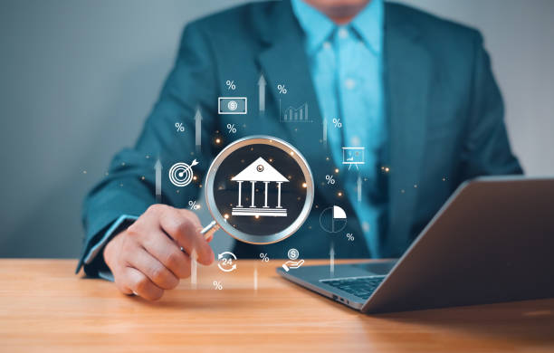 istock Businessman analyzing digital financial data on a laptop, with a magnifying glass focusing on a bank icon and various financial symbols. 2204734510