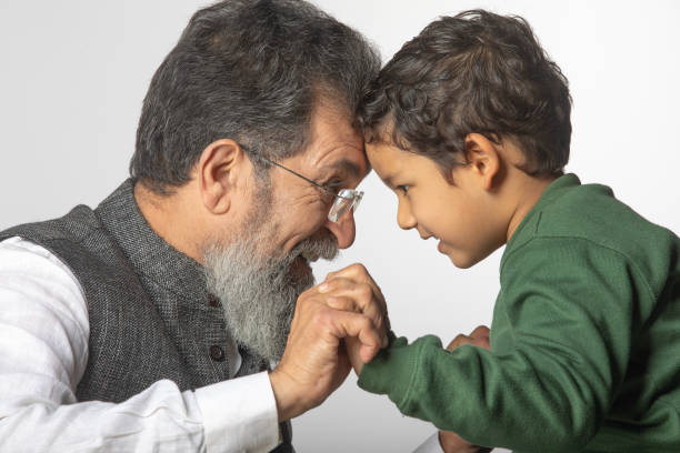 Side view of playful senior grandfather and cute grandson with face to face holding hands and fighting against white background