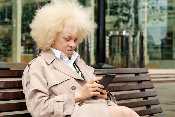 istock Albino businesswoman using mobile phone while sitting on bench 2204735975