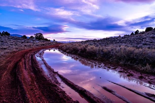 4x4 Mountain Dirt Road with Mud and Puddles with Sunset Reflections - Scenic high elevation area in late winter, early spring with melting snow and large puddles filled with muddy water reflecting colorful sunset skies.