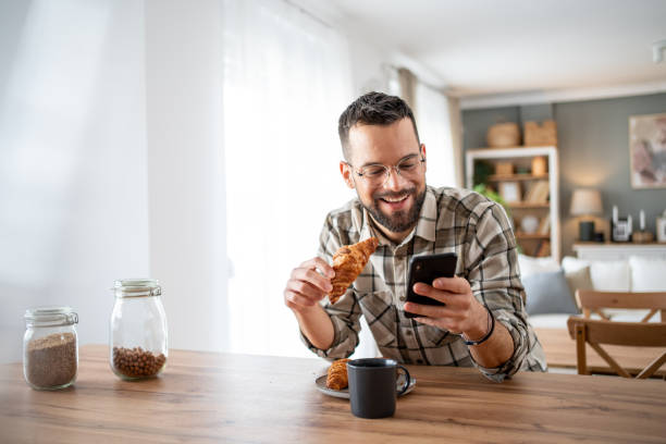 istock Happy man eating breakfast and using his phone at home 2204740104