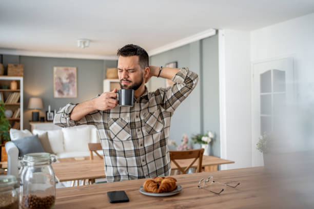 istock Sleepy man drinking coffee and stretching at breakfast counter 2204740282