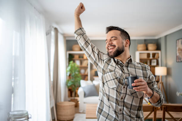 istock Happy man stretching and drinking coffee in living room 2204740325