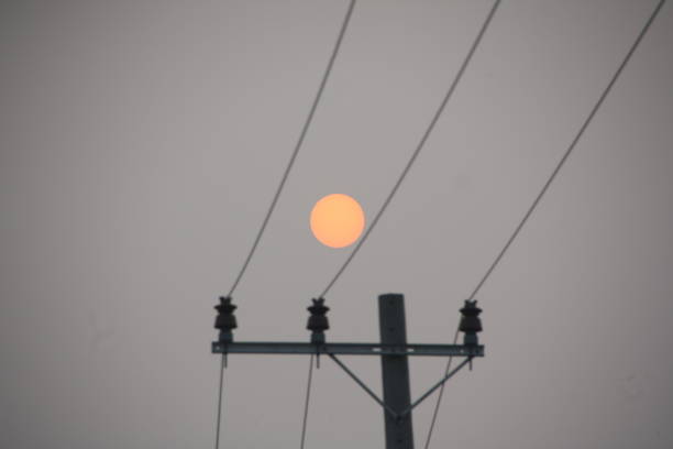 The sunrise slowly rises above the electric pole, creating a dramatic silhouette in the morning sky. Its golden light embraces the stretching cables, forming a harmony between nature’s beauty and the marks of human progress.