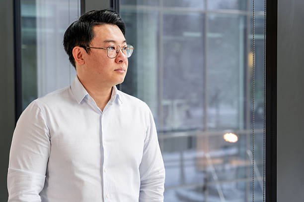 istock Businessman Standing in Office, Looking Confident and Thoughtful by Window 2204745795