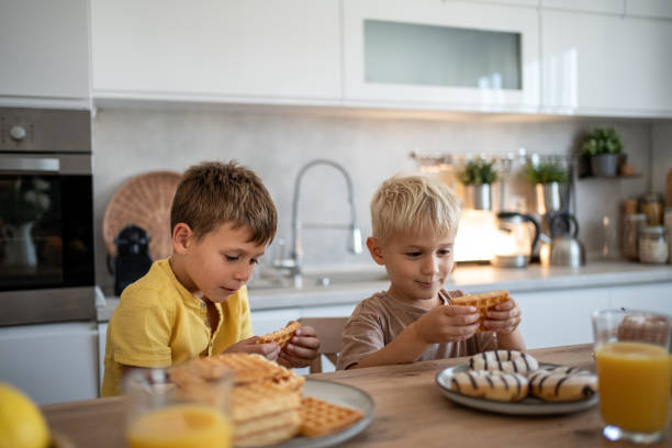 istock Two brothers eating waffles and donuts for breakfast in a modern kitchen 2204747814