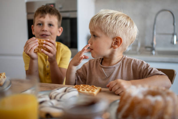 istock Two brothers eating waffles and pastries for breakfast in a modern kitchen 2204747849