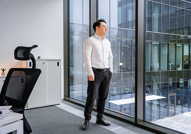 istock Asian Businessman Looking Out Office Window in Modern Workplace 2204748620