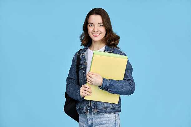istock Pretty student girl holding notebooks and looking at camera, isolated on blue background. 2204749163