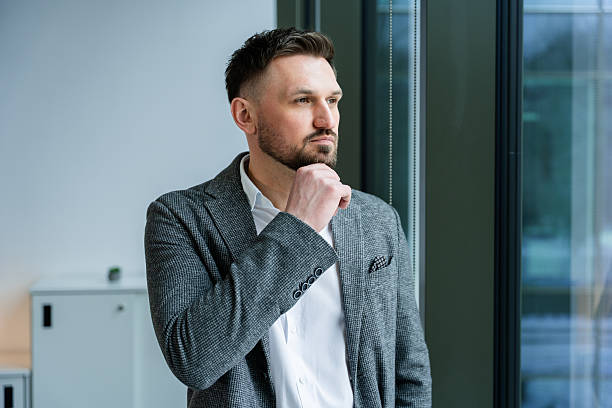 istock Professional Businessman in Thoughtful Pose Looking Through Office Window 2204749813