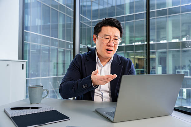 istock Confused Businessman Gesturing While Working on Laptop in Modern Office 2204751349