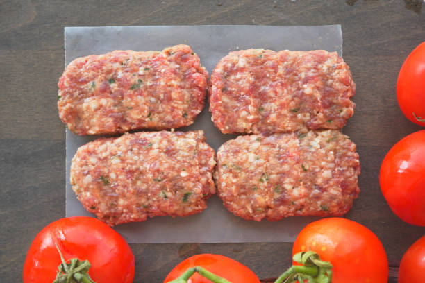 istock Raw Meat Patties with Fresh Tomatoes are beautifully displayed on a Rustic Wooden Surface 2204752220