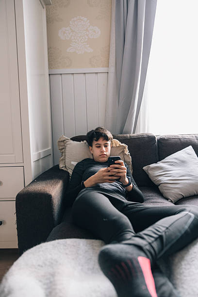 istock Teenager lying on sofa using smartphone in winter time 2204756646