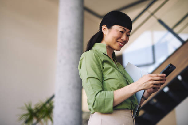 istock Japanese businesswoman using smartphone and holding documents in office building 2204758379