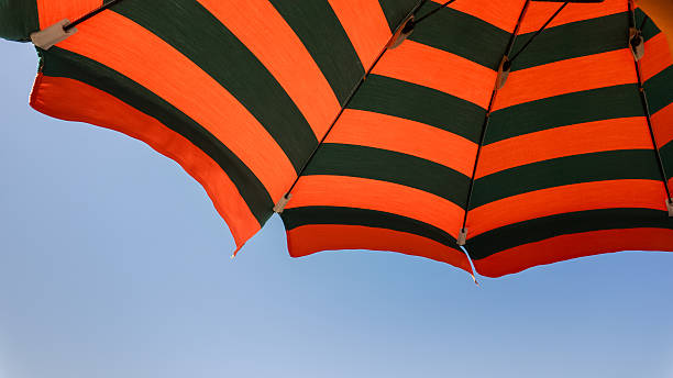 istock Orange and green beach umbrellas. Blue sky. Relaxing context. View from below. Summer holidays at the sea. General contest and location 2204758881