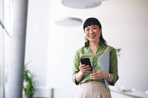 istock Japanese businesswoman using smartphone and holding folder in office 2204758884