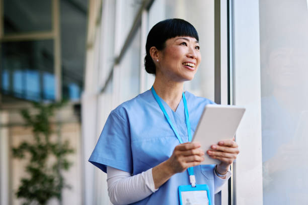 istock Japanese Nurse looking outside a window holding a tablet and smiling 2204759039