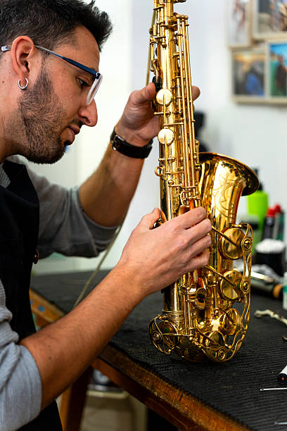 istock Luthier carefully repairing keys of saxophone in workshop 2204760052