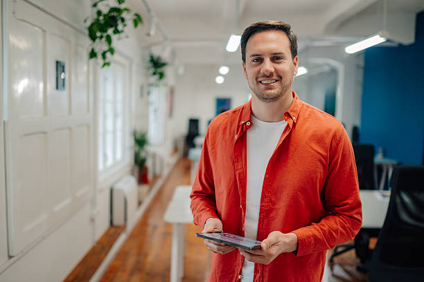 istock Startup businessman holding digital tablet and smiling at camera in modern office 2204767531