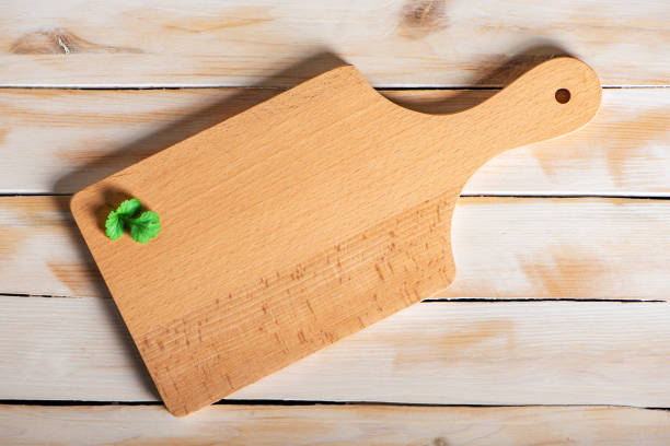 Gastronomic concept, cutting board with cilantro leaves on a white rustic wooden table, top view.