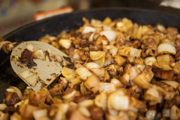 A pan of food with a spoon in it. The food is a mix of meat and onions