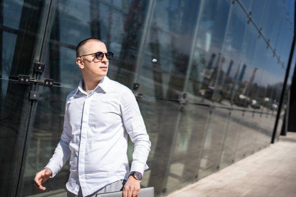 Business individual in formal wear walking by an architectural glass facade, exuding professionalism and determination. Perfect for themes of modern work culture and outdoor professional environment.