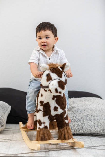 A happy toddler enjoys a playful ride on a plush rocking horse, capturing the joy of childhood imagination and early motor skill development.