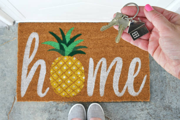 New house real estate concept keys by front door welcome mat Female holding a set of house keys on keychain over a welcome mat that says Home with a pineapple. key doormat stock pictures, royalty-free photos & images