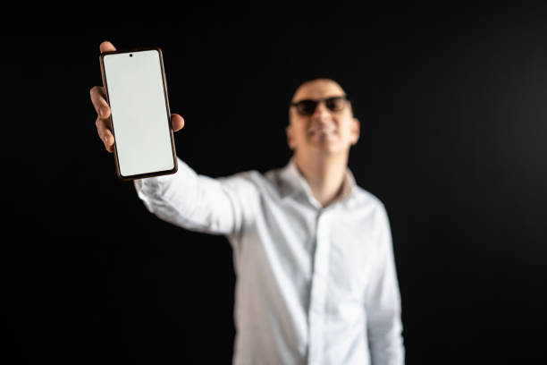 istock Man Holding Smartphone with Blank Screen Against Dark Background 2204782399