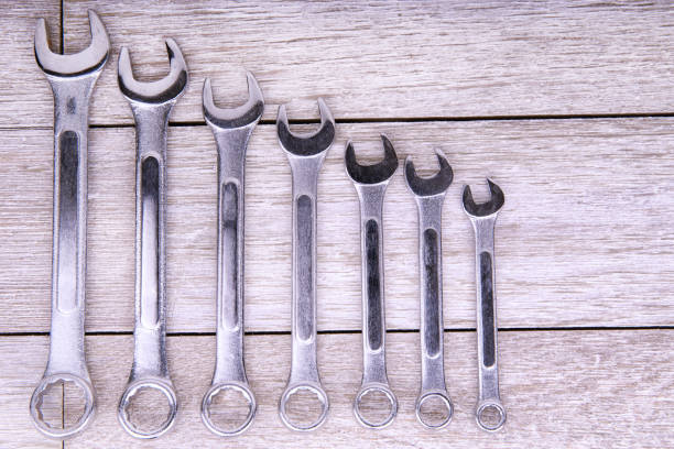 Set of metallic wrenches arranged in size order on a rustic wooden background. Ideal for themes related to mechanics, construction, DIY projects, and professional toolkits in industrial settings.