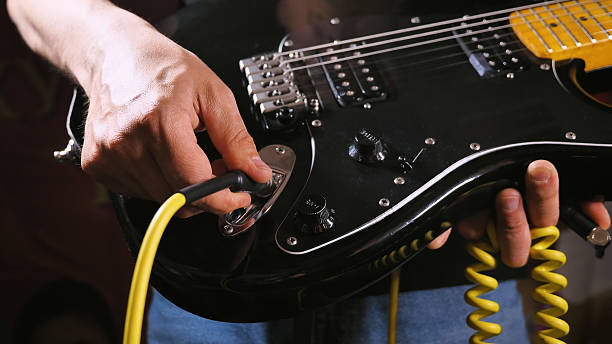 istock A person is plugging a yellow coiled cable into a black electric guitar. The guitar has a glossy finish, visible strings, and control knobs. 2204808393