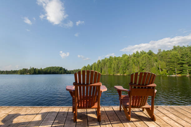 istock Two Adirondack chairs on a dock, facing a calm Muskoka lake. 2204814734