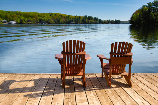 istock Adirondack chairs on a dock, facing a rippling Muskoka lake and cabins. 2204814757