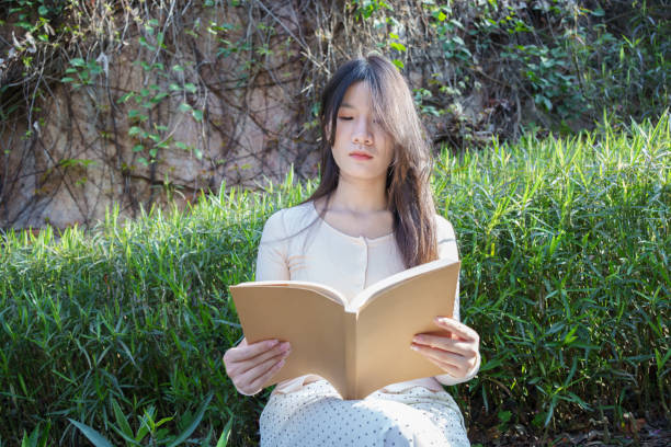 Asian woman sitting outdoors reading a book