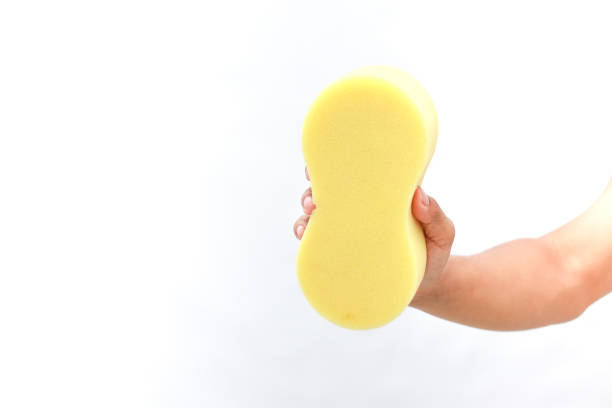Hand holding a yellow sponge on a white background. Cleaning, washing concept