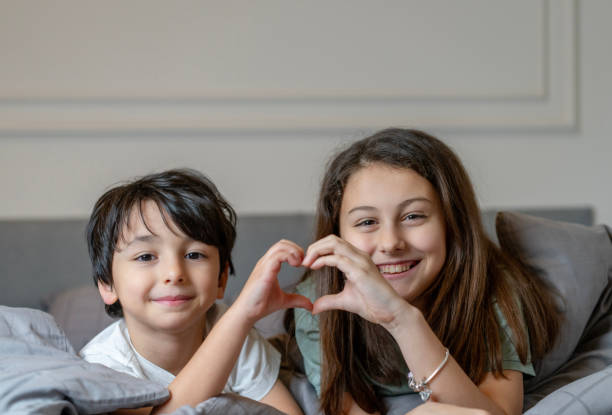 istock Siblings in bed making a heart shape with hands, close up portrait 2204827045