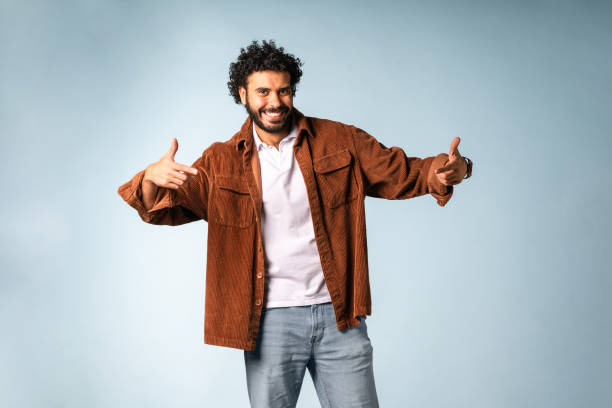 istock Smiling Middle Eastern Man in Casual Outfit Gesturing Confidently Against Light Blue Background 2204829786