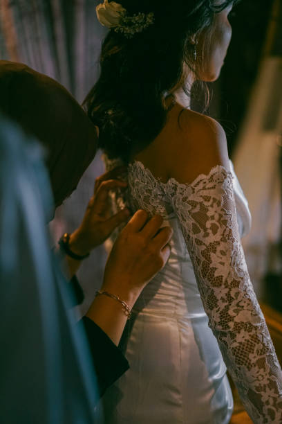 istock Bride Getting Ready as Attendant Adjusts Elegant Lace Wedding Dress 2204832491
