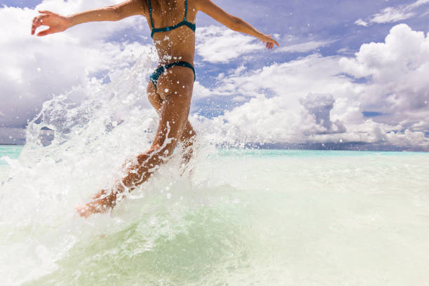 istock Playful woman splashing water while running through sea. 2204835866