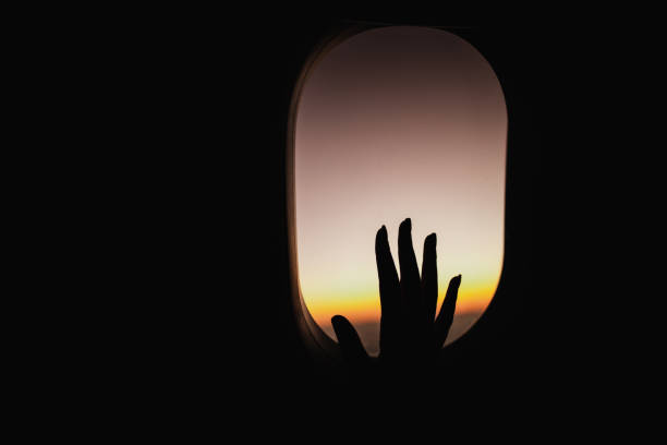 istock Silhouette of a woman's hand on an airplane window at sunset. 2204836400