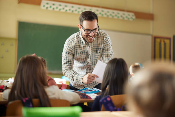istock Happy male teacher assisting his student on a class at elementary school. 2204837700